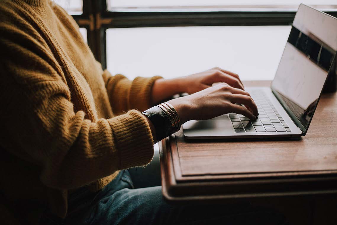 Close-up of woman typing on Apple MacBook at table.